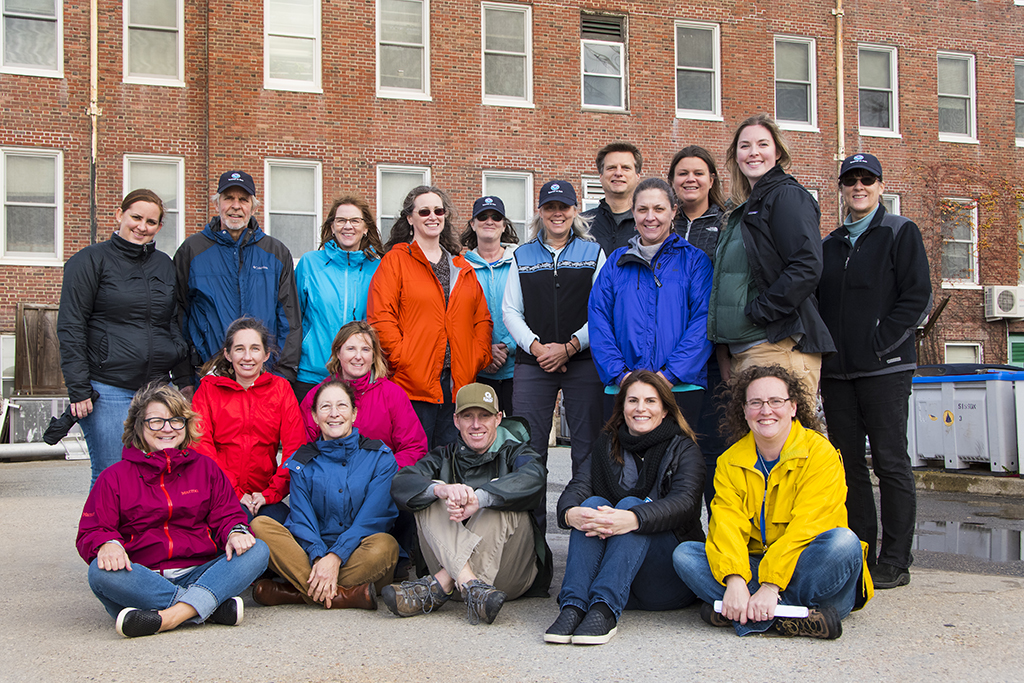 Several adults wearing winter jackets pose in rows for a photo outside.