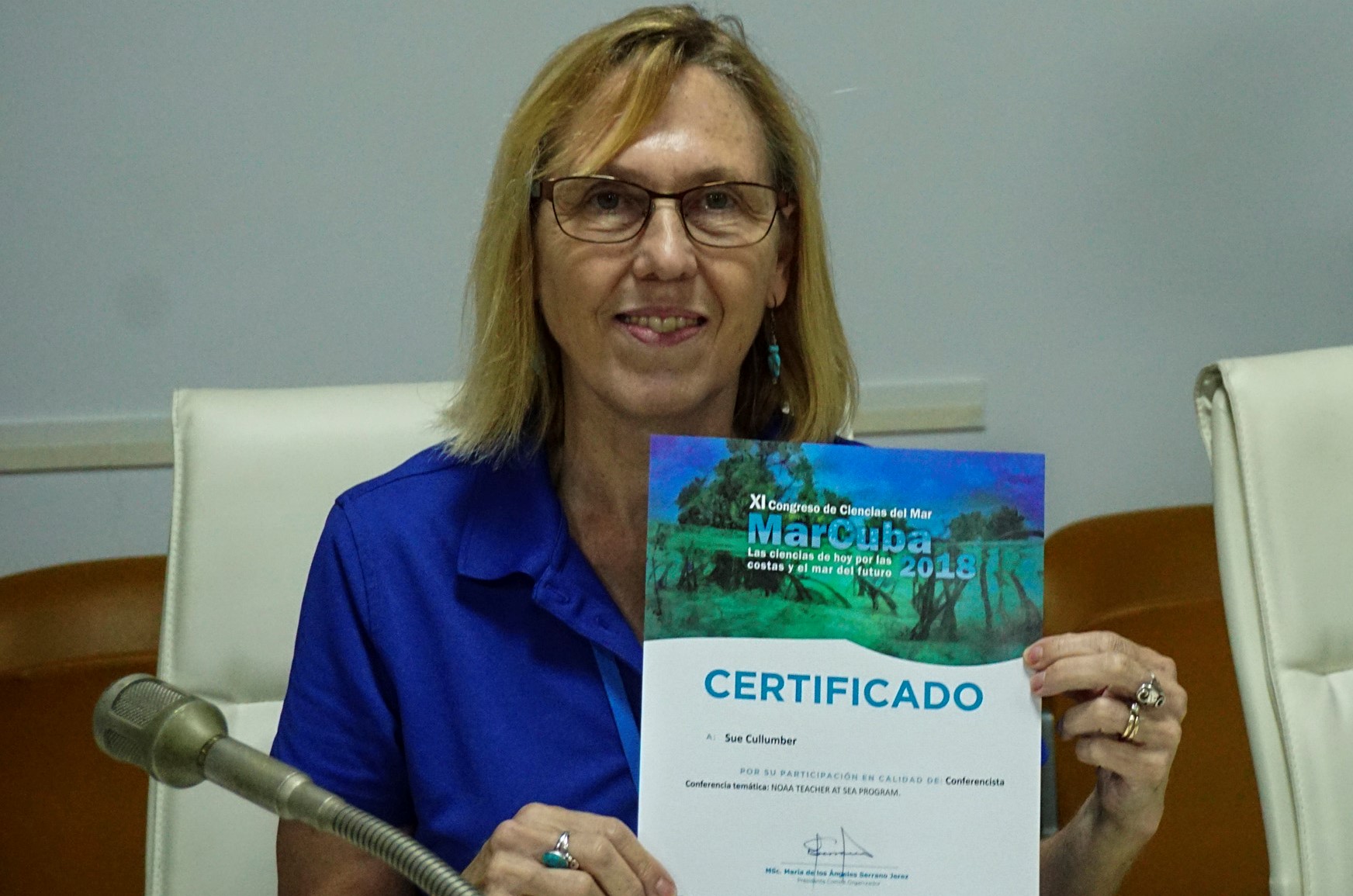 A woman in a blue shirt holds up a certificate.