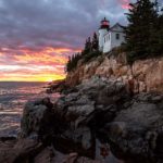 Image of lighthouse on rocky coast with sunrise.