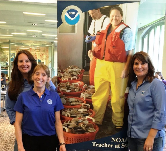Three women stand in front of a tall NOAA Teacher at Sea sign.