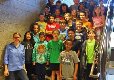 A woman is standing at the front of a stairway going up with five rows of children on each step going up the stairway.