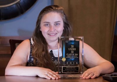 A woman is sitting at a table with an award for the "30 Under 30" for 2016 in front of her.