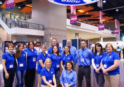 A group of men and woman stand in the NOAA booth in a large conference center. The NOAA logo is hanging above them.