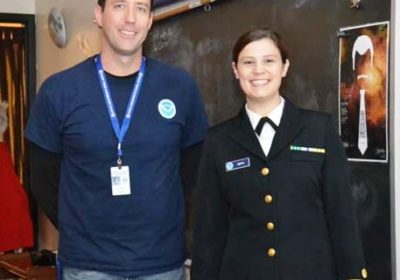 A man and a woman in a military uniform stand in a classroom.