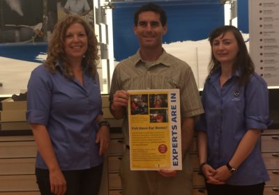 Two women and one man stand together while the man holds a sign.