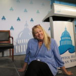 A woman sits in front of a Capito Hill Ocean Week sign.