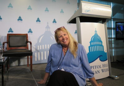 A woman sits in front of a Capito Hill Ocean Week sign.