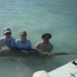 Three people standing in the water holding a smalltooth sawfish.