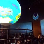 A class of students sitting listening to a presentation with a large sphere in the center.