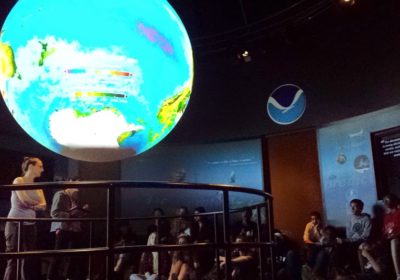 A class of students sitting listening to a presentation with a large sphere in the center.