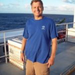 A man on a ship with the water in the background.