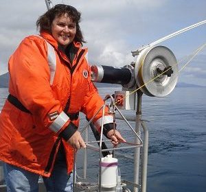 A woman standing on board a ship with water in the background.
