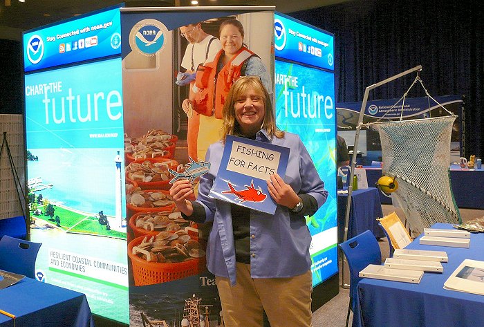 A woman stands in front of a NOAA sign holding a Fishing for Facts sign.