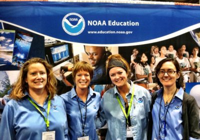 Four women stand in front of a NOAA Education sign.