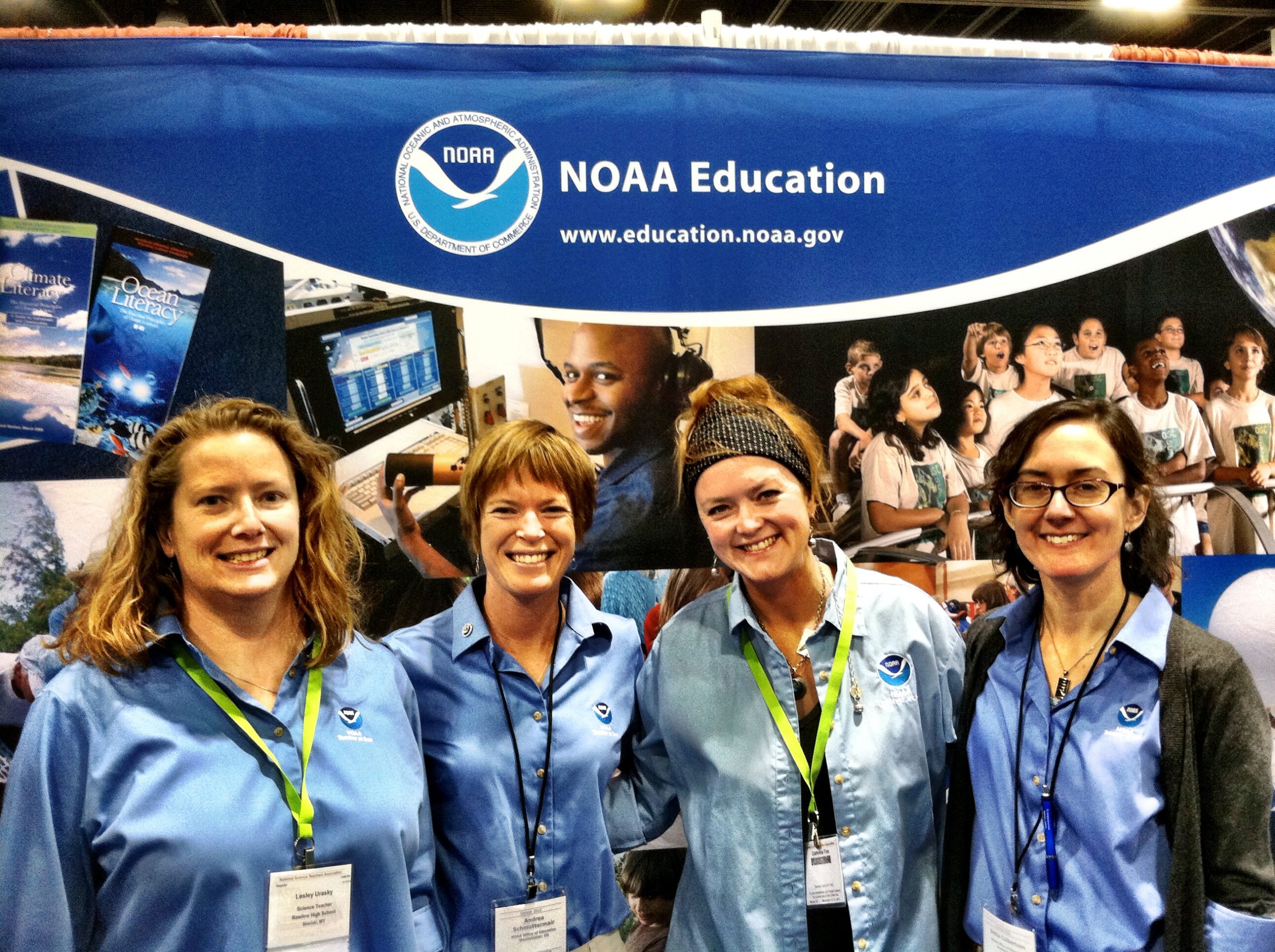 Four women stand in front of a NOAA Education sign.
