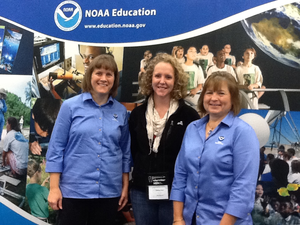 Three women stand in front of a NOAA Education sign.