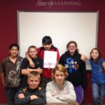 Seven students gathered together while one of them holds a picture.