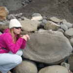 A woman is kneeling by rocks and looking off into the distance.