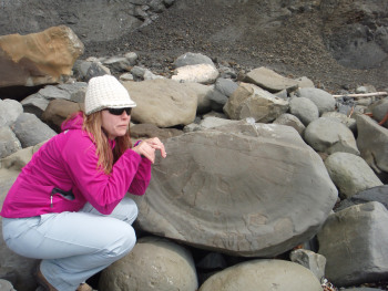 A woman is kneeling by rocks and looking off into the distance.