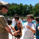 A woman in a military uniform is speaking to a group of students in front of an outdoor pool.
