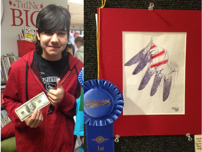 A young student stands next to his artwork that has a big blue ribbon on it.