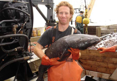 A man on a ship holding a fish with fish and another man in the background.