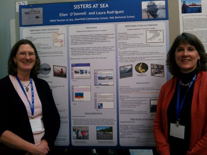 Two women stand in front of a sign that says "Sisters at Sea".