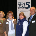 Three women and one man stand in front of a Cape Cod 5 Foundation sign.