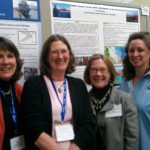 Four women stand in front of a NOAA Teacher at Sea sign.