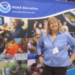 A woman stands in front of a NOAA Education sign.