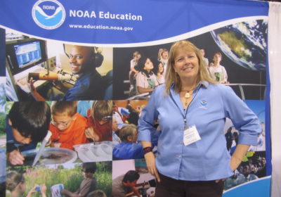 A woman stands in front of a NOAA Education sign.