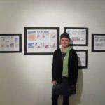 A woman stands in front of several cartoon drawings hanging on the wall.