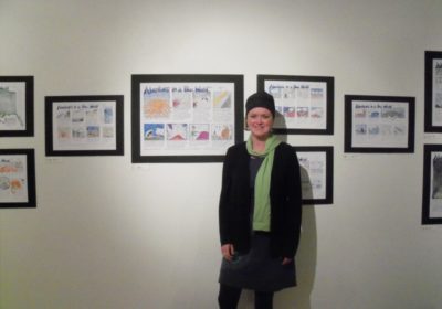 A woman stands in front of several cartoon drawings hanging on the wall.