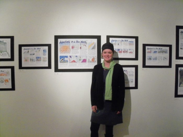 A woman stands in front of several cartoon drawings hanging on the wall.