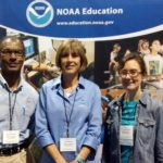 A man and two women stand in front of a NOAA Education sign.