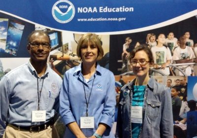 A man and two women stand in front of a NOAA Education sign.