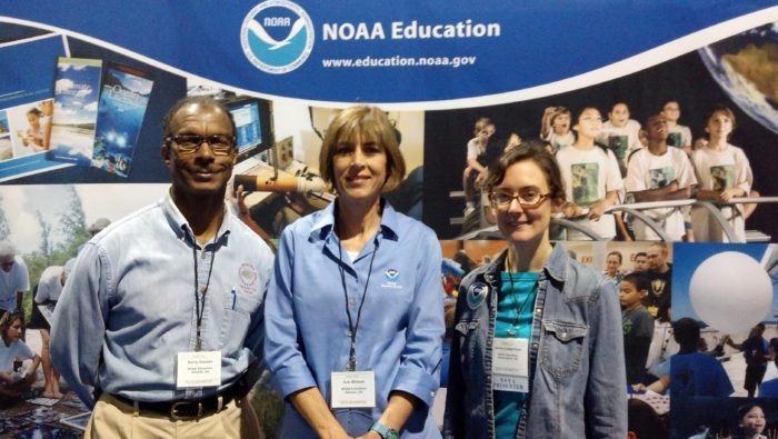 A man and two women stand in front of a NOAA Education sign.