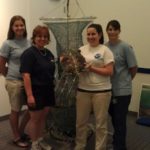 Four woman stand together with one of them holding a turtle.