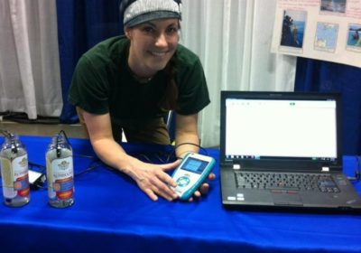 A person standing behind a NOAA table that has a laptop and they are holding a conductivity probe.