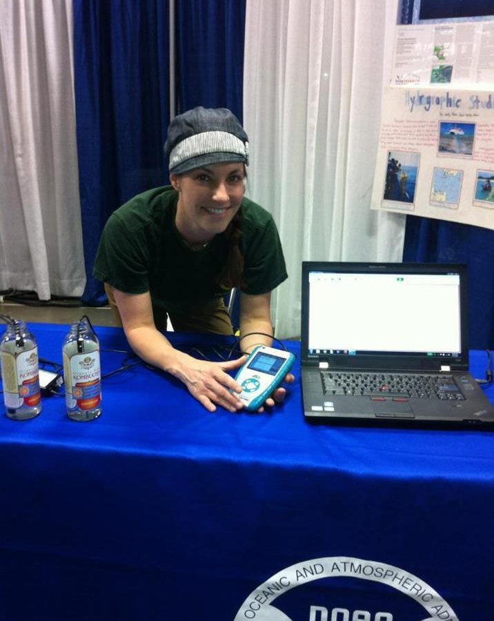 A person standing behind a NOAA table that has a laptop and they are holding a conductivity probe.