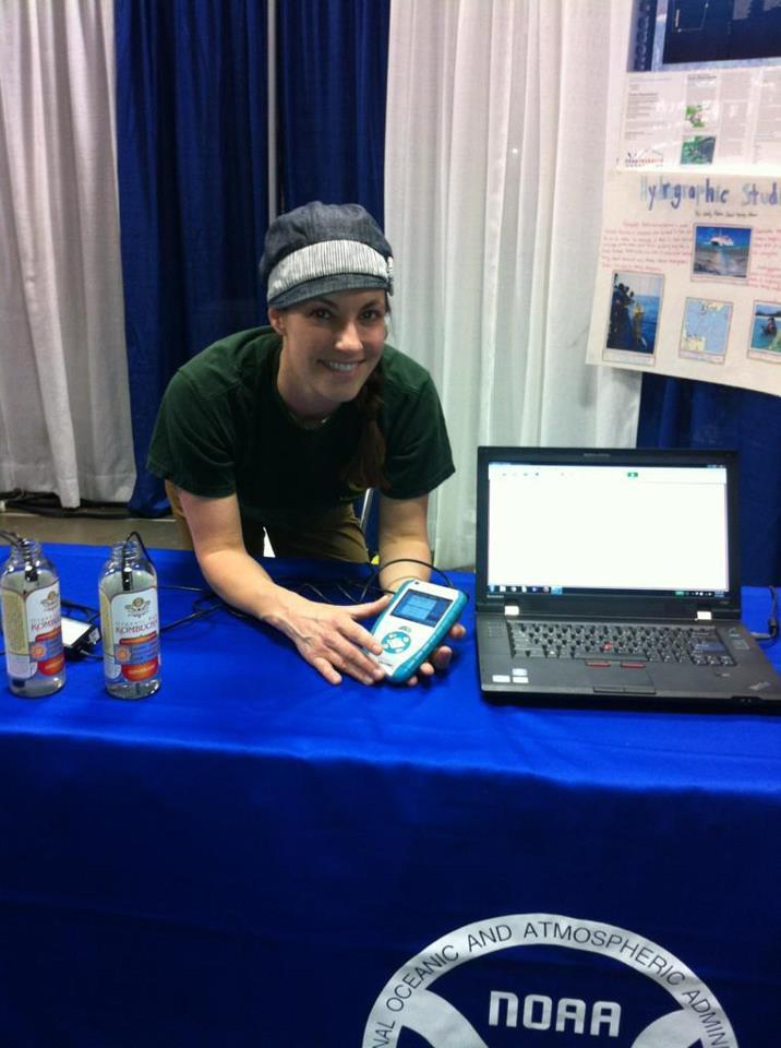 A person standing behind a NOAA table that has a laptop and they are holding a conductivity probe.