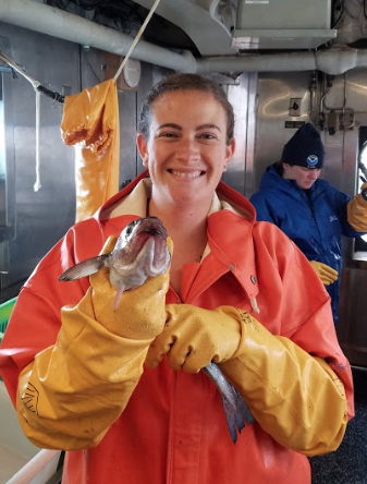 A woman in orange rain slickers holding a pollock with yellow rubber gloves.