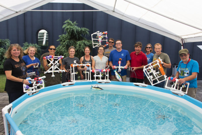 Several educators stand around a small pool, holding their remotely operated vehicles that were designed and built in a workshop.