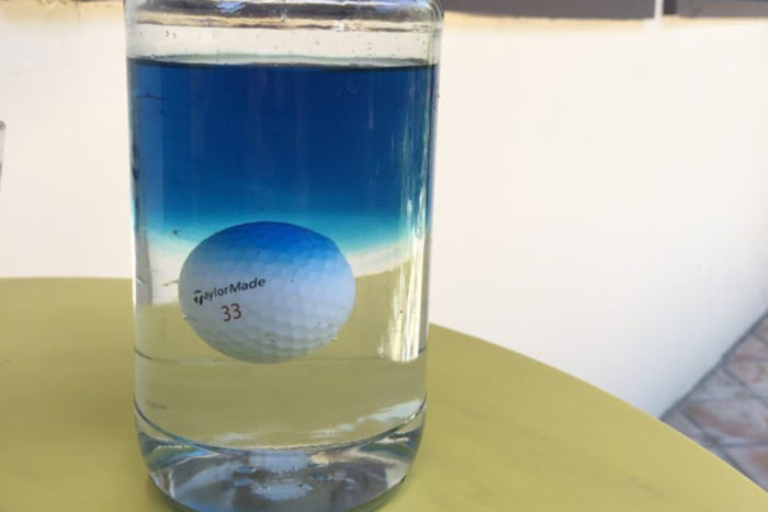 Golf ball floating in glass of water with blue dye at the top