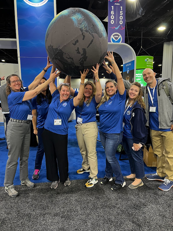 Staff holding giant earth model at NOAA booth at 2023 NSTA