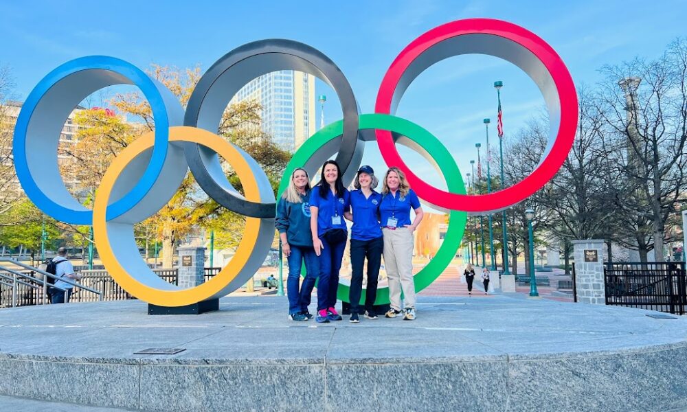 Four teachers in blue shirt standing in front of Olympic rings sculpture in Atlanta