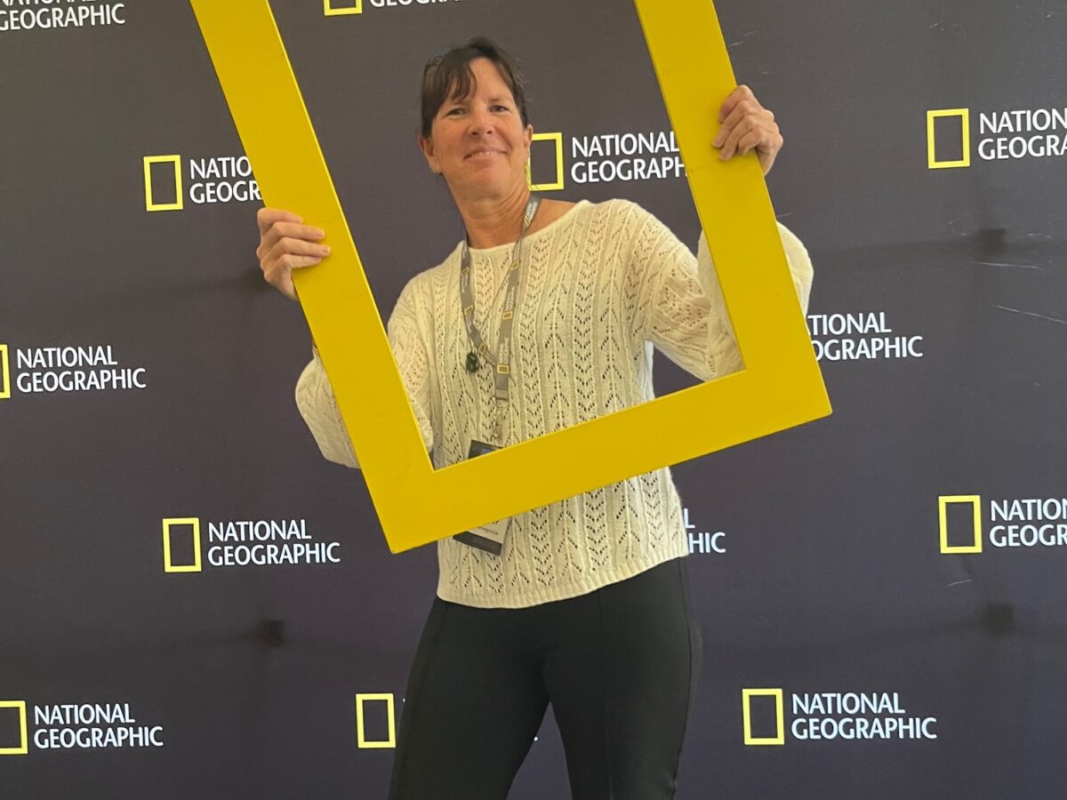 Woman holding life sized National Geographic yellow frame around her head and standing in front of National Geographic banners backdrop