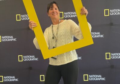Woman holding life sized National Geographic yellow frame around her head and standing in front of National Geographic banners backdrop