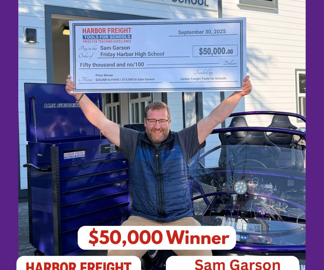A man smiles and raises his arms in victory while holding a large $50,000 STEAM Educator Award check from Harbor Freight Tools for Schools outside Friday Harbor High School, next to a blue vehicle.